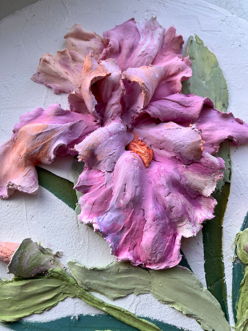 K&ouml;nnte beinhalten: Nahaufnahme einer dreidimensionalen, pinkfarbenen und orangefarbenen Iris-Bl&uuml;te mit gr&uuml;nen Bl&auml;ttern. Die Bl&uuml;te ist texturiert und scheint aus Ton zu sein.
