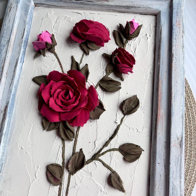 May include: A framed wall art piece featuring a 3D sculpted floral design with pink and red roses on a textured white background.