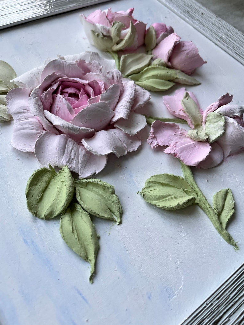Peut inclure: Une &oelig;uvre d'art murale 3D encadr&eacute;e repr&eacute;sentant des roses roses et blanches avec des feuilles vertes. Les roses sont sculpt&eacute;es et ont une texture r&eacute;aliste.
