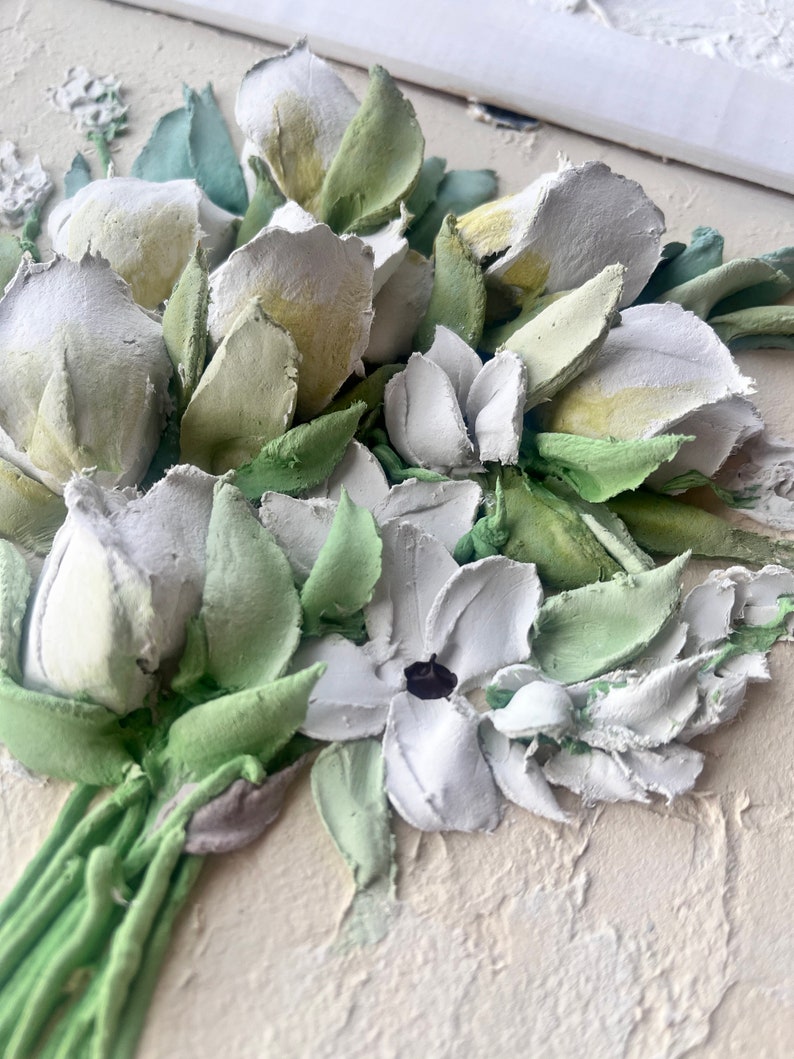 May include: A close-up of a 3D floral painting featuring white and green flowers. The flowers are crafted from textured paint and appear to be arranged in a bouquet.