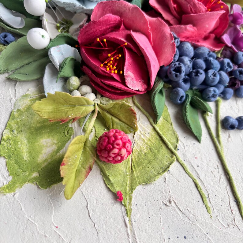 May include: Close-up of a floral arrangement featuring vibrant red roses, blueberries, and green leaves. The artwork has a textured, white background, and the flowers have yellow stamens. The arrangement includes white berries and a raspberry.