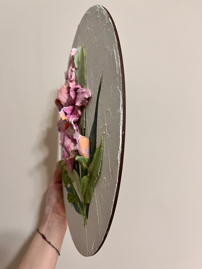 K&ouml;nnte beinhalten: Ein rundes, strukturiertes Leinwandbild einer rosa und orangefarbenen Blume mit gr&uuml;nen Bl&auml;ttern. Das Bild ist auf einem Holzrahmen.