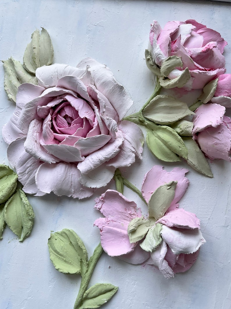 Peut inclure: Une &oelig;uvre d'art murale 3D repr&eacute;sentant des roses roses et blanches avec des feuilles vertes. Les roses sont sculpt&eacute;es dans un style r&eacute;aliste et semblent &ecirc;tre faites de pl&acirc;tre ou d'argile.