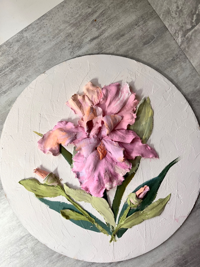 K&ouml;nnte beinhalten: Eine rosa und orangefarbene Iris-Blume mit gr&uuml;nen Bl&auml;ttern, die auf eine runde Leinwand gemalt ist.