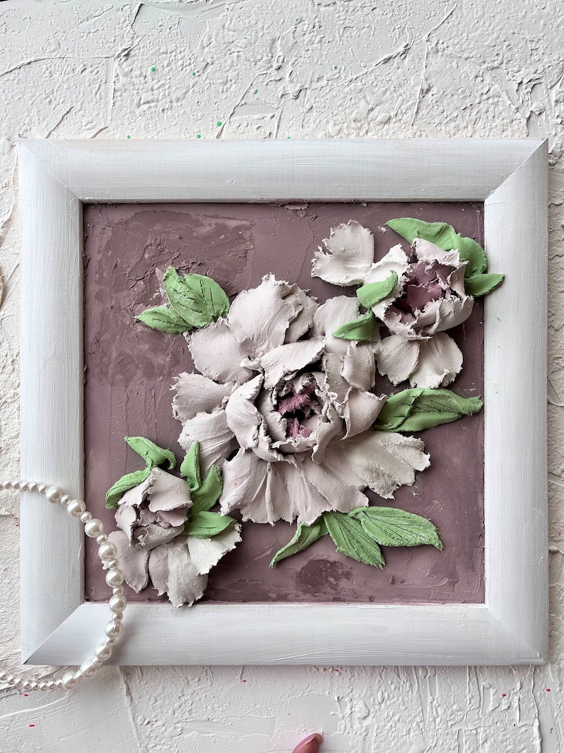 May include: A framed artwork featuring a 3D relief sculpture of white peonies with green leaves on a light brown background.