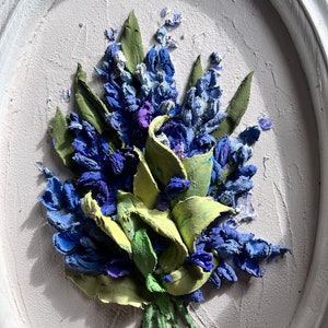 May include: A close-up of a 3D painting depicting a bouquet of blue and green flowers. The flowers are painted in a realistic style and have a textured surface.