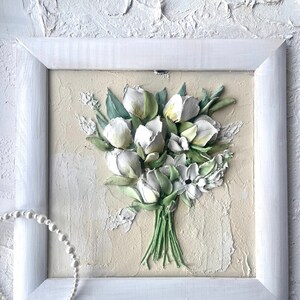 May include: A white framed painting of a bouquet of white flowers with green stems and leaves on a textured beige background.