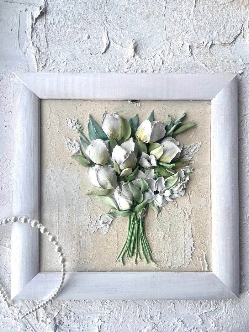May include: A white framed painting of a bouquet of white flowers with green stems and leaves on a textured beige background.