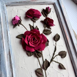 May include: A framed wall art piece featuring a 3D sculpted design of pink and red roses with brown stems and leaves.
