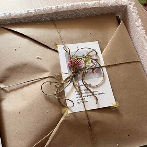May include: A wrapped package with a floral artwork, tied with twine. A tag with the title "Roses" and artist information is attached. The artwork is 40x40 inches, with a textured paste medium, created in 2023.
