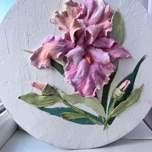 K&ouml;nnte beinhalten: Eine rosa und wei&szlig;e Iris-Blume mit gr&uuml;nen Bl&auml;ttern ist auf einer runden wei&szlig;en Leinwand gemalt. Die Blume ist texturiert und wirkt dreidimensional.