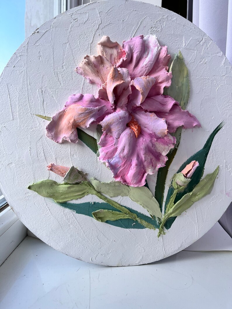 K&ouml;nnte beinhalten: Eine rosa und wei&szlig;e Iris-Blume mit gr&uuml;nen Bl&auml;ttern ist auf einer runden wei&szlig;en Leinwand gemalt. Die Blume ist texturiert und wirkt dreidimensional.