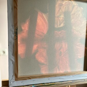 Puede incluir: Un primer plano de una pintura sobre lienzo con un marco de madera. La pintura presenta un dise&ntilde;o suave y abstracto de flores rosas y blancas. El lienzo est&aacute; estirado sobre el marco y asegurado con grapas.