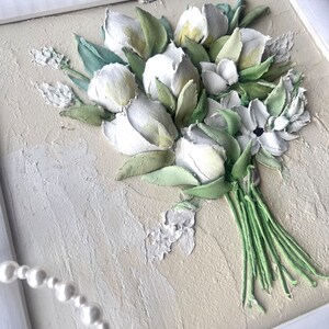 May include: A white framed painting of a bouquet of white flowers with green leaves. The flowers are painted in a 3D style, giving the impression of texture.