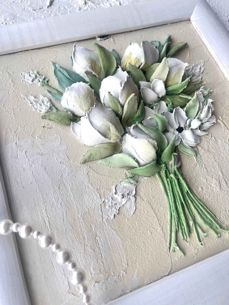May include: A white framed painting of a bouquet of white flowers with green leaves. The flowers are painted in a 3D style, giving the impression of texture.