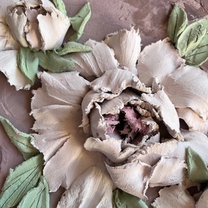 May include: Close-up of a white, textured, 3D flower with green leaves. The flower is made of a material that resembles clay or plaster.