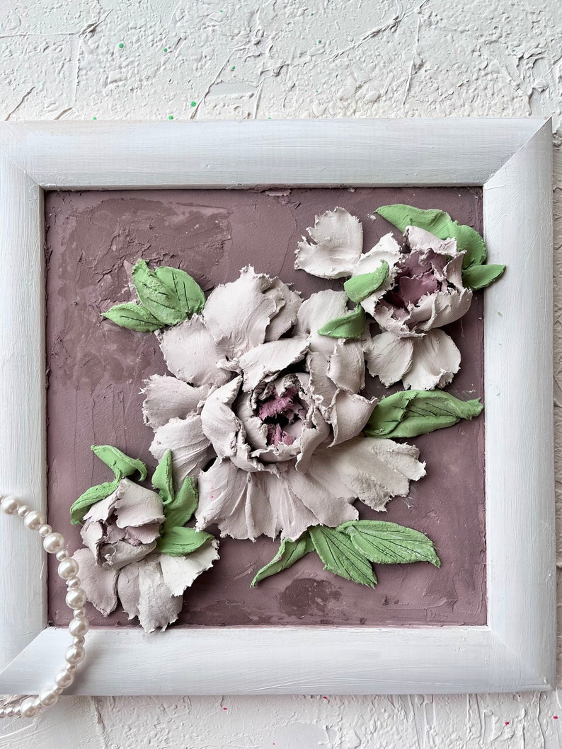 May include: A framed 3D art piece featuring a bouquet of white peonies with green leaves on a textured mauve background.