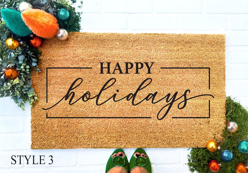 May include: A brown coir doormat with the text "HAPPY holidays" in a black cursive font inside a black rectangular frame.