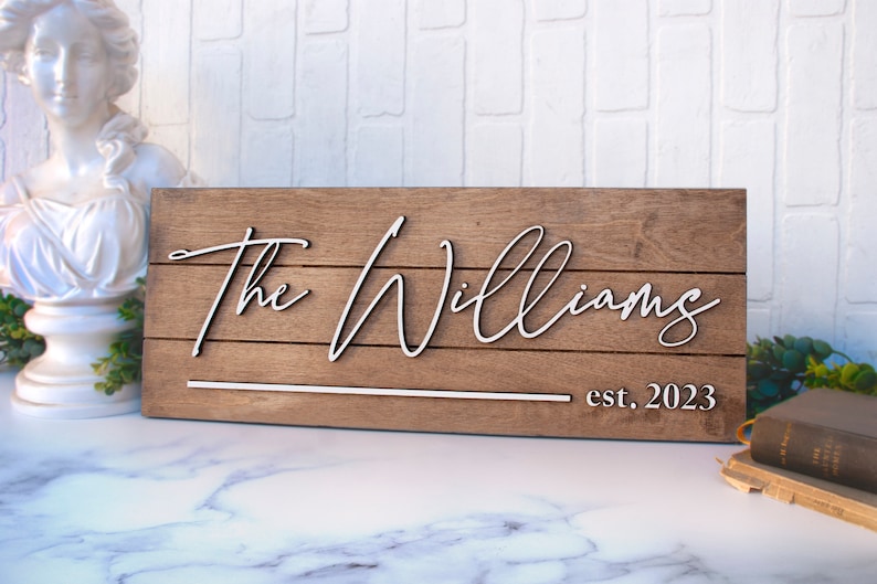 May include: A wooden sign with the text "The Williams est. 2023" in white raised lettering.
