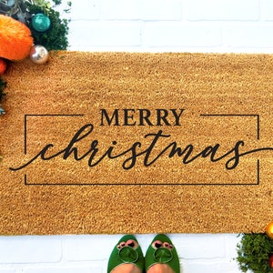 May include: A brown coir doormat with the text "Merry Christmas" in black lettering inside a black frame.