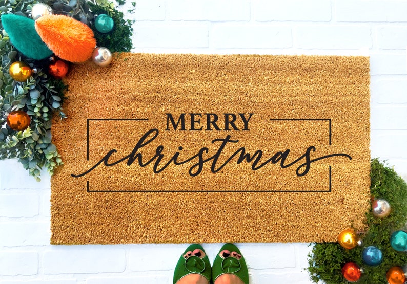 May include: A brown coir doormat with the text "Merry Christmas" in black lettering inside a black frame.