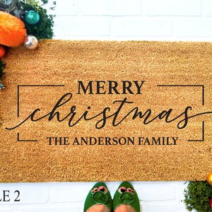May include: A brown coir doormat with the text "Merry Christmas" in a black cursive font with a black border. The text "The Anderson Family" is printed below the greeting.