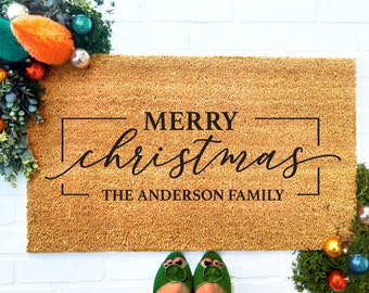 May include: A brown coir doormat with the text "Merry Christmas" in a black cursive font inside a black frame. Below the text is "The Anderson Family" in black text.