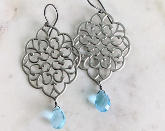 May include: Silver filigree earrings with teardrop shaped blue gemstone accents.