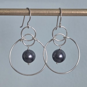 May include: Silver hoop earrings with a black pearl dangling from each hoop.