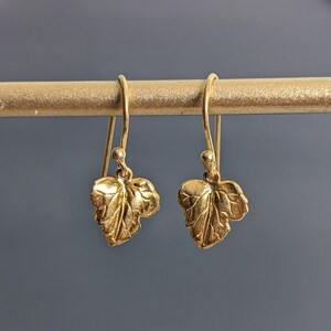 May include: A pair of gold-toned earrings with a leaf design. The earrings are hanging from a gold-toned bar.