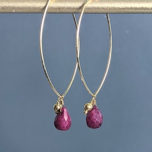 May include: Gold hoop earrings with a dangling ruby gemstone and gold bead accents.