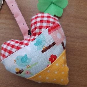 Può includere: Un portachiavi a forma di cuore rosso e bianco a quadri con un pannello in tessuto blu e bianco con uccelli e un pannello in tessuto giallo con pois bianchi.