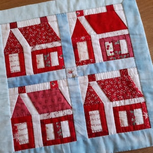 Puede incluir: Una colcha de retazos azul y blanca con un diseño de casas rojas y blancas. Las casas tienen techos rojos y ventanas blancas. La colcha tiene el texto "A Part of Me Is In Every Good Wish I Send You" y "Thankful Hearts Are So Warm We Want To Share Our's With You".