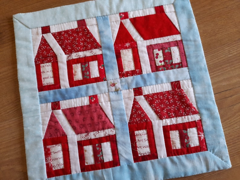 May include: A blue and white patchwork quilt with a red and white house design. The houses have red roofs and white windows. The quilt has the text "A Part of Me Is In Every Good Wish I Send You" and "Thankful Hearts Are So Warm We Want To Share Our's With You".
