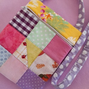 Peut inclure: Un sac à main en tissu patchwork avec une fermeture éclair et une bandoulière à pois. Le sac est fait de différentes couleurs et motifs, dont le rose, le vert, le jaune et le bleu.