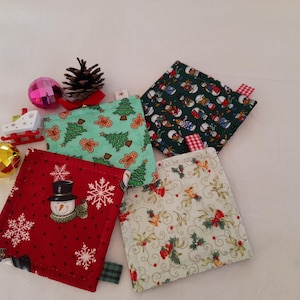 Può includere: Quattro sottobicchieri in tessuto a tema natalizio con vari motivi, tra cui pupazzi di neve, omini di pan di zenzero, alberi di Natale e agrifoglio. Sono presenti anche decorazioni natalizie come palline e una pigna.