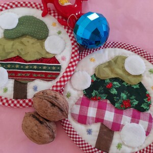 Può includere: Due sottobicchieri fatti a mano a forma di albero di Natale con bordo a quadri rossi e bianchi. I sottobicchieri sono realizzati in tessuto e presentano un design patchwork in tessuto verde, rosso e bianco. I sottobicchieri sono circondati da noci.