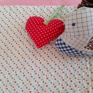 May include: A white fabric with a pattern of small blue and brown stars. A red heart-shaped pillow with white polka dots and a blue and white plaid pillow are on the fabric.