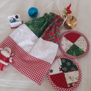 Può includere: Una borsa a cordoncino a quadri rossi e bianchi con un design a patchwork verde e rosso. La borsa è decorata con una piccola statuetta di Babbo Natale e due sottobicchieri rotondi a patchwork con disegni rossi, verdi e bianchi.