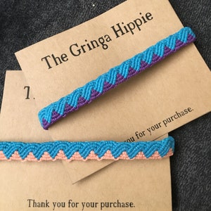 May include: Two handmade friendship bracelets with a chevron pattern. The top bracelet is blue and purple, and the bottom bracelet is blue and pink. The bracelets are on a brown card with the text "The Gringa Hippie" and "Thank you for your purchase."
