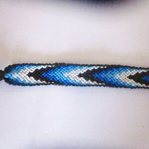May include: A blue, white, and black friendship bracelet with a chevron pattern.
