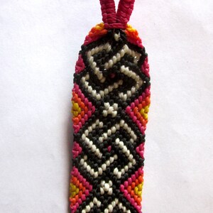 Peut inclure: Un bracelet d'amitié coloré avec un motif géométrique noir, blanc, rose, orange et jaune. Le bracelet a une boucle rose en haut pour une fixation facile.