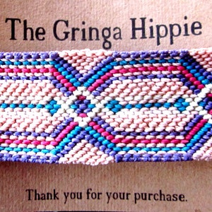 May include: A pink, purple, blue, and white woven friendship bracelet with the text "The Gringa Hippie" and "Thank you for your purchase." on a brown card.