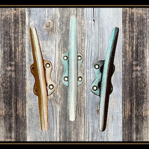 May include: Three metal boat cleats in different colors: teal, brown, and blue. The cleats are mounted on a wooden wall.