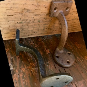 Puede incluir: Dos soportes de estante de hierro fundido con un acabado marr&oacute;n r&uacute;stico. Los soportes tienen un dise&ntilde;o curvo y est&aacute;n montados en una superficie de madera.