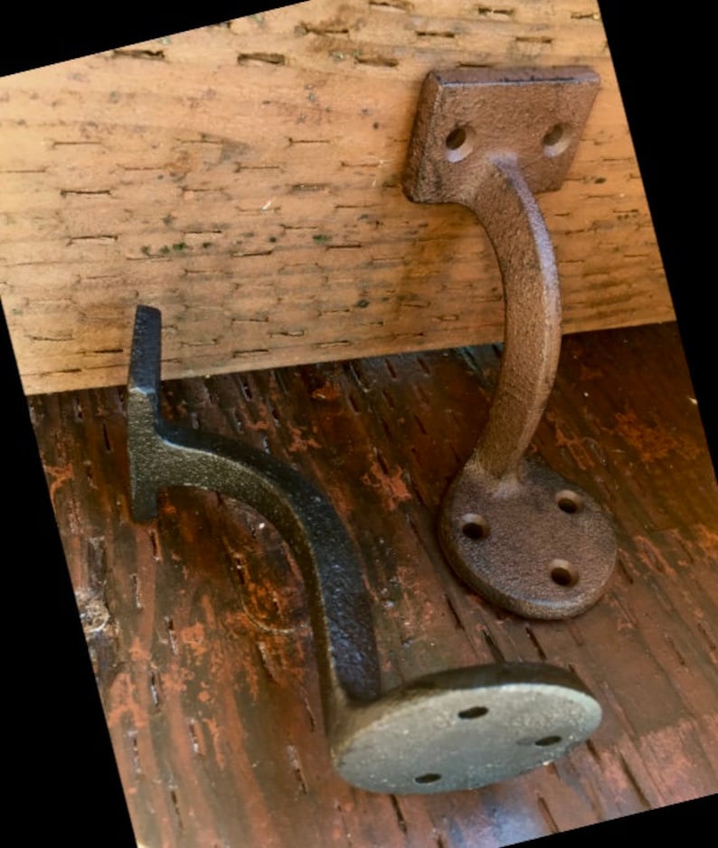 Puede incluir: Dos soportes de estante de hierro fundido con un acabado marr&oacute;n r&uacute;stico. Los soportes tienen un dise&ntilde;o curvo y est&aacute;n montados en una superficie de madera.