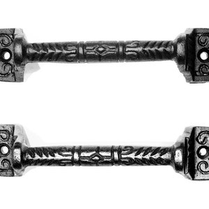 May include: Two black cast iron drawer pulls with ornate designs. Each pull has a square end with a floral design and a center hole. The center section of the pull has a repeating leaf pattern.