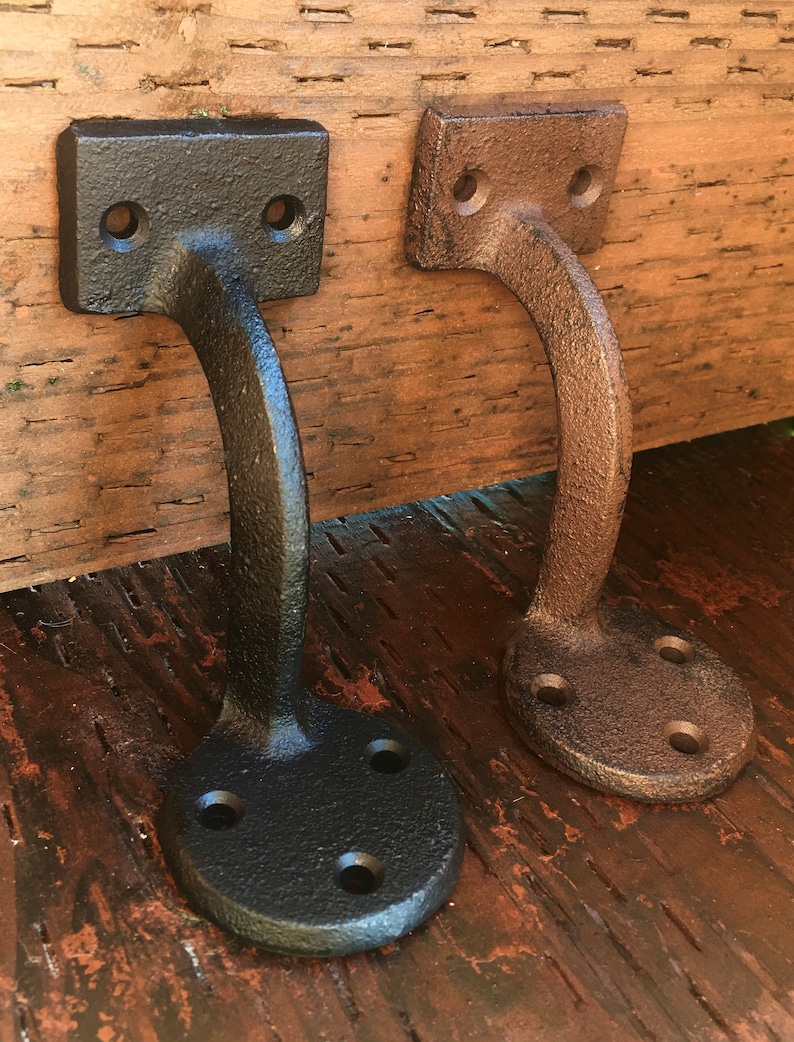 Puede incluir: Dos soportes de estante de hierro fundido, uno negro y otro marr&oacute;n, con un dise&ntilde;o curvo y una base redonda. Los soportes est&aacute;n montados en una superficie de madera.