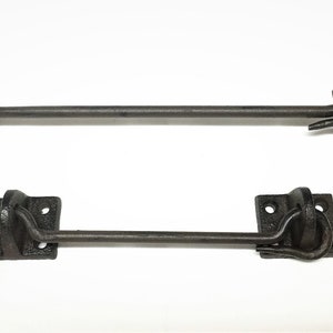 May include: Two black metal door latch hooks with square plates and a curved hook. The hooks are attached to a metal rod.