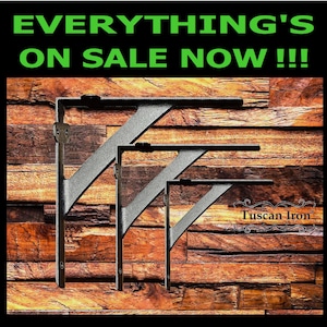 May include: Three black metal shelf brackets of different sizes against a wood background. The largest bracket is at the top and the smallest is at the bottom. The text "Tuscan Iron" is visible in the lower right corner of the image.